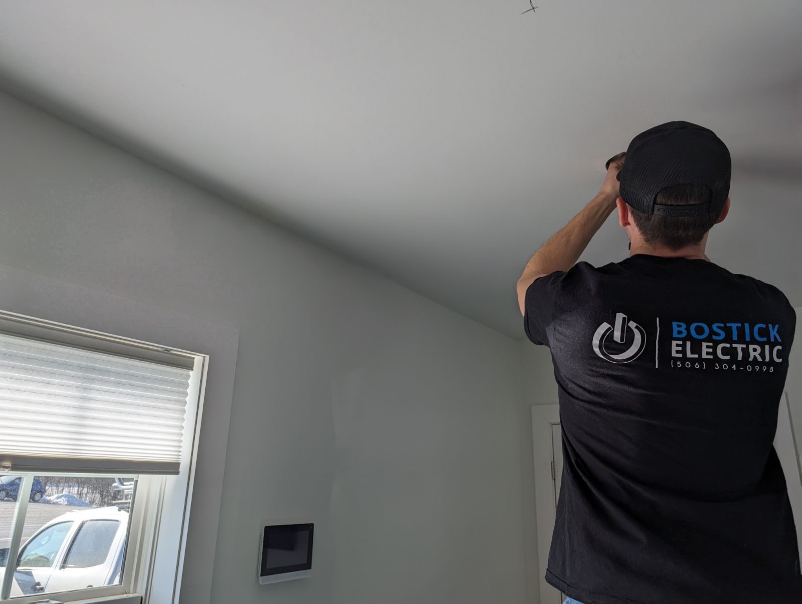 Bostick Electric technician installing on a ceiling in a Fredericton home, wearing a branded Bostick Electric uniform